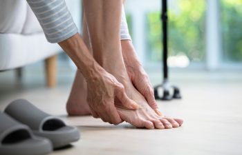 Foot pain concept, senior woman suffering from pain in ankle at home. woman rubbing, massaging sore feet area of pain, Mature woman discomfort painful feet ache from walking.