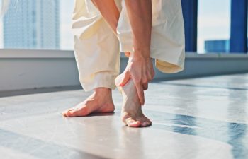 Injury, legs and dancer in studio, hurt and fracture on ankle, joint pain and accident for person. Tension, hands and sore on foot, muscle and inflammation for performer, bone and fitness in Japan.